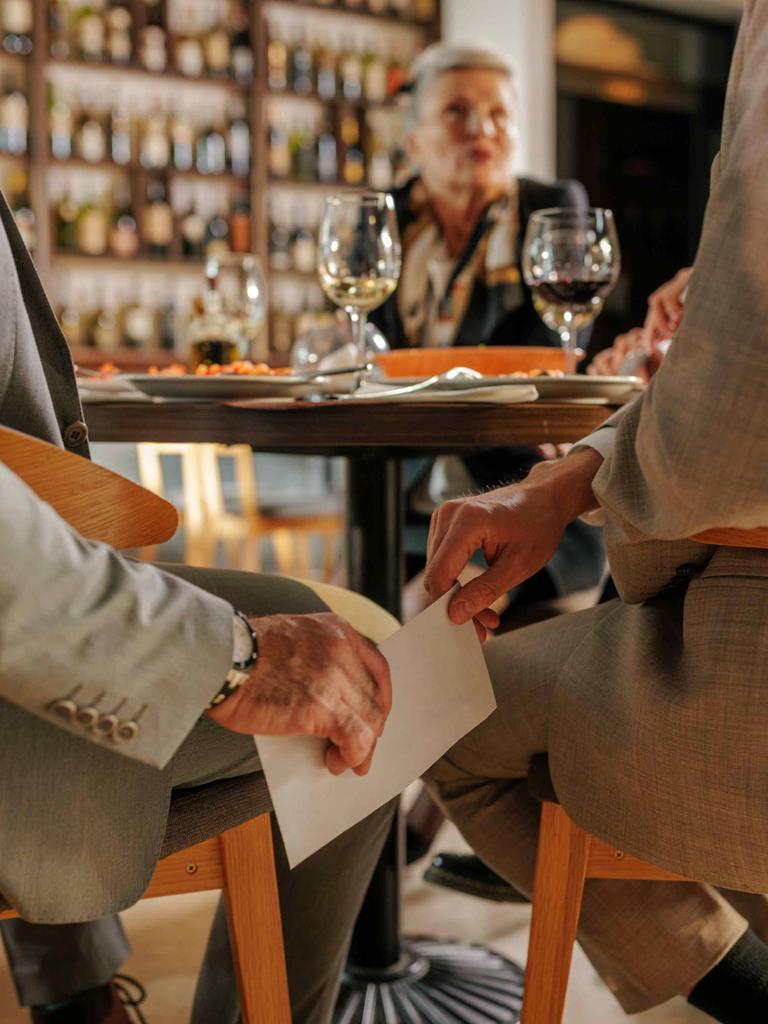 In einem Restaurant reicht ein Mann dem anderen unter dem Tisch einen weißen Umschlag. In einem Restaurant reicht ein Mann dem anderen unter dem Tisch einen weißen Umschlag.