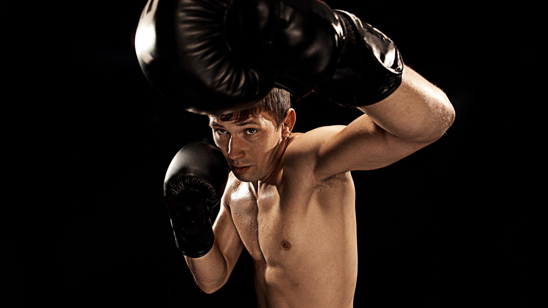 Studioaufnahme eines männlichen Boxers, der in Richtung der Kamera schlägt und versucht sich mit der anderen Hand zu schützen.