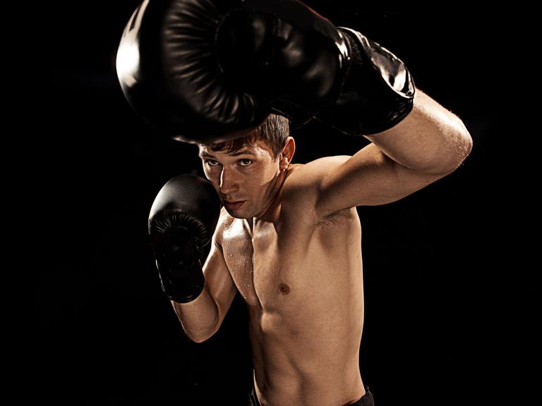 Studioaufnahme eines männlichen Boxers, der in Richtung der Kamera schlägt und versucht sich mit der anderen Hand zu schützen.