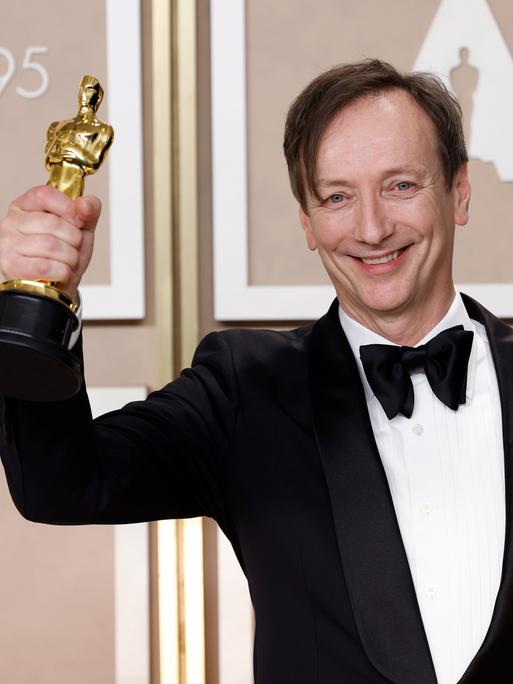 Der Komponist Volker Bertelmann hält die Oscar-Trophäe in der Hand. 