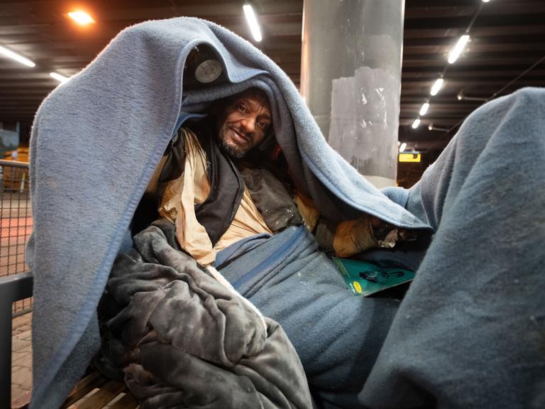 Obdachlose Person  auf einer Bank am U-Bahnhof Galluswarte bedeckt sich mit einer Decke