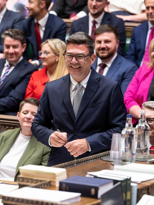 Andy Burnham steht während seiner Vereidigung als Abgeordneter im britischen Unterhaus und lächelt. Andy Burnham steht während seiner Vereidigung als Abgeordneter im britischen Unterhaus und lächelt.