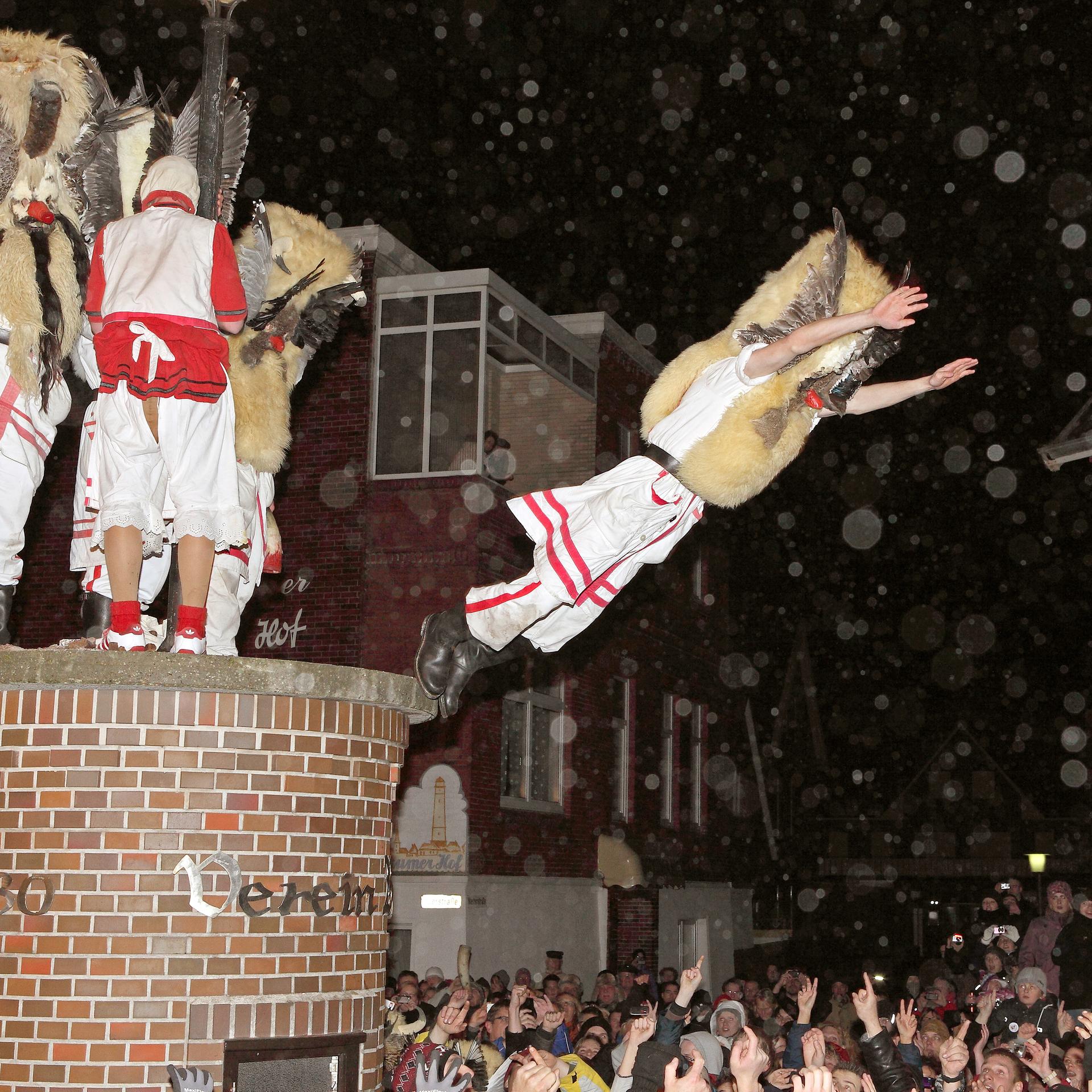 Mit Masken verkleidete Männer des Vereins Borkumer Jungens stürzen sich am Abend (Aufnahme vom 05.12.2011) in der Innenstadt der Nordseeinsel von einer LitfaÃsäule in die Arme der Schaulustigen.
