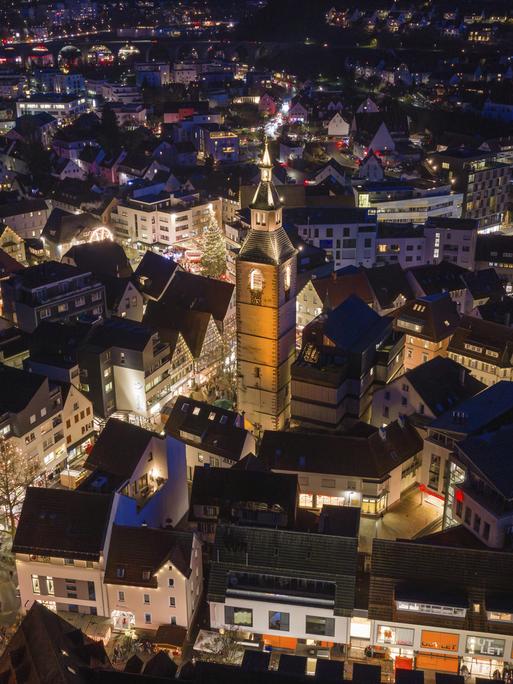 Luftaufnahme einer beleuchteten Stadt bei Nacht, dominiert von einer großen Kirche, umgeben von festlich beleuchteten Häusern.