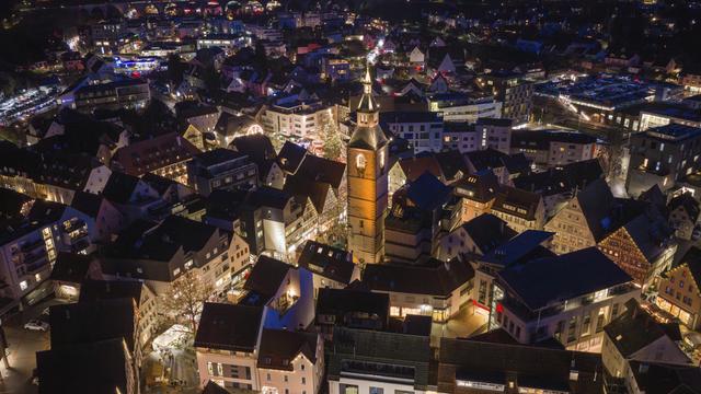 Luftaufnahme einer beleuchteten Stadt bei Nacht, dominiert von einer großen Kirche, umgeben von festlich beleuchteten Häusern. Luftaufnahme einer beleuchteten Stadt bei Nacht, dominiert von einer großen Kirche, umgeben von festlich beleuchteten Häusern.