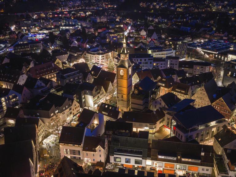 Luftaufnahme einer beleuchteten Stadt bei Nacht, dominiert von einer großen Kirche, umgeben von festlich beleuchteten Häusern.