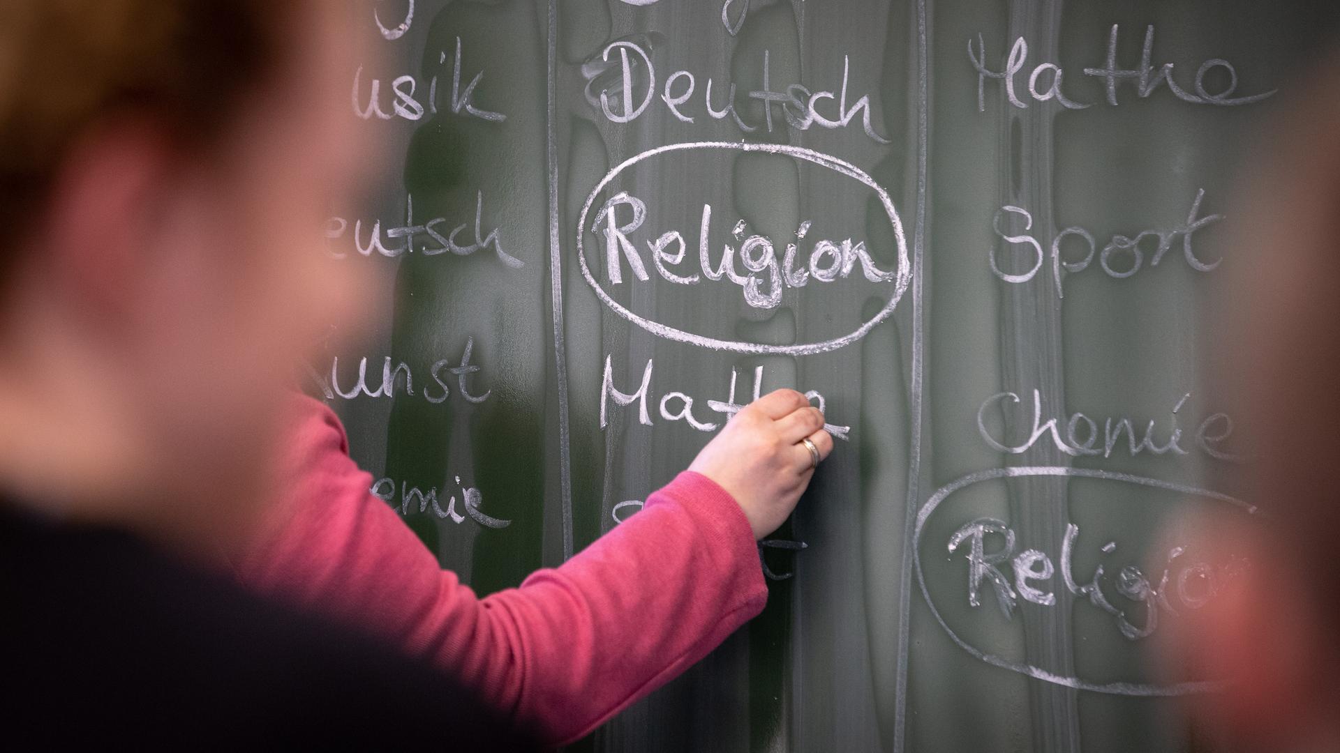 Eine Schülerin an der Tafel, auf der mit Kreide das Wort "Religion" geschreiben steht