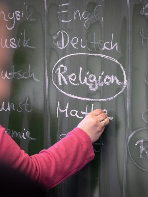 Eine Schülerin an der Tafel, auf der mit Kreide das Wort "Religion" geschreiben steht