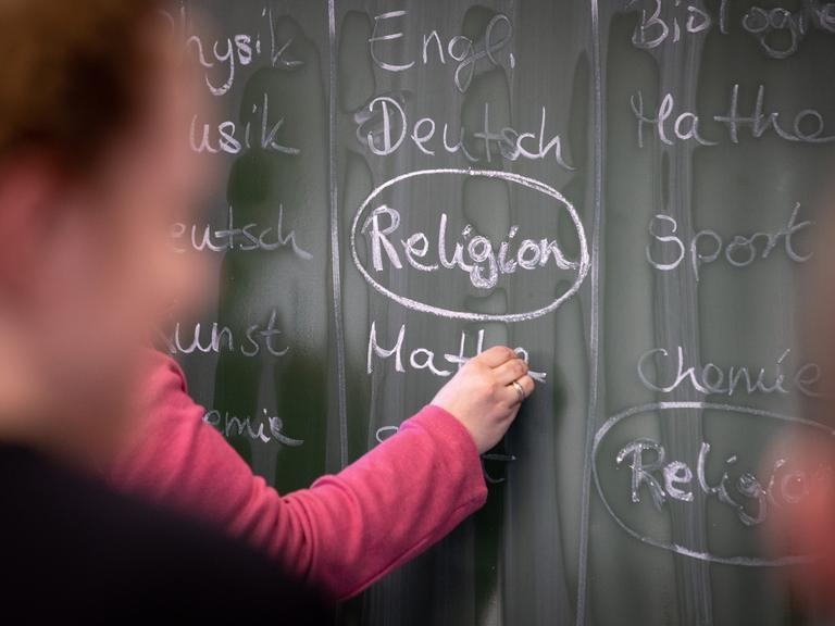 Eine Schülerin an der Tafel, auf der mit Kreide das Wort "Religion" geschreiben steht