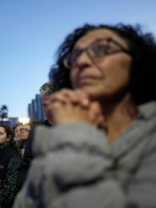 Menschen stehen vor Hochhäusern beieinander. Eine Frau im Vordergrund hat die Hände wie für ein Gebet gefaltet. Es sind Angehörige von Geiseln der Hamas.