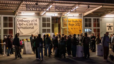 Abendaufnahme einer Halle, an der "Körber Studio" zu lesen ist. Davor stehen Menschen und unterhalten sich. 