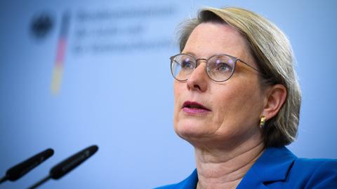 Stefanie Hubig spricht bei einer Pressekonferenz vor einem hellblauen Hintergrund in ein Mikrofon. 