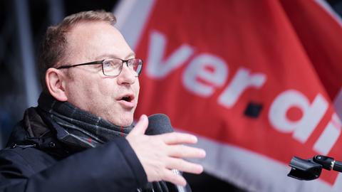 Der Verdi-Vorsitzende Frank Werneke steht vor einer Fahne mit dem Verdi-Logo und spricht in ein Mikrofon.
