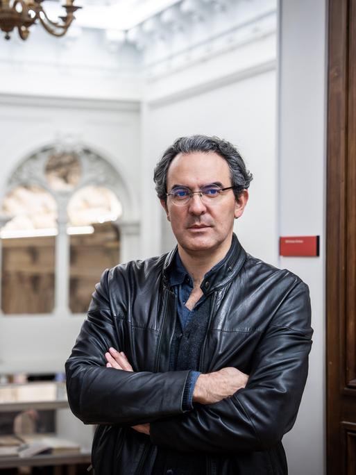 Juan Gabriel Vásquez steht in einem palastartigen Gebäude, seine Arme sind verschränkt