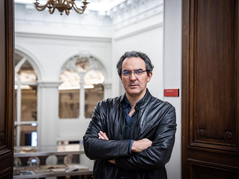 Juan Gabriel Vásquez steht in einem palastartigen Gebäude, seine Arme sind verschränkt
