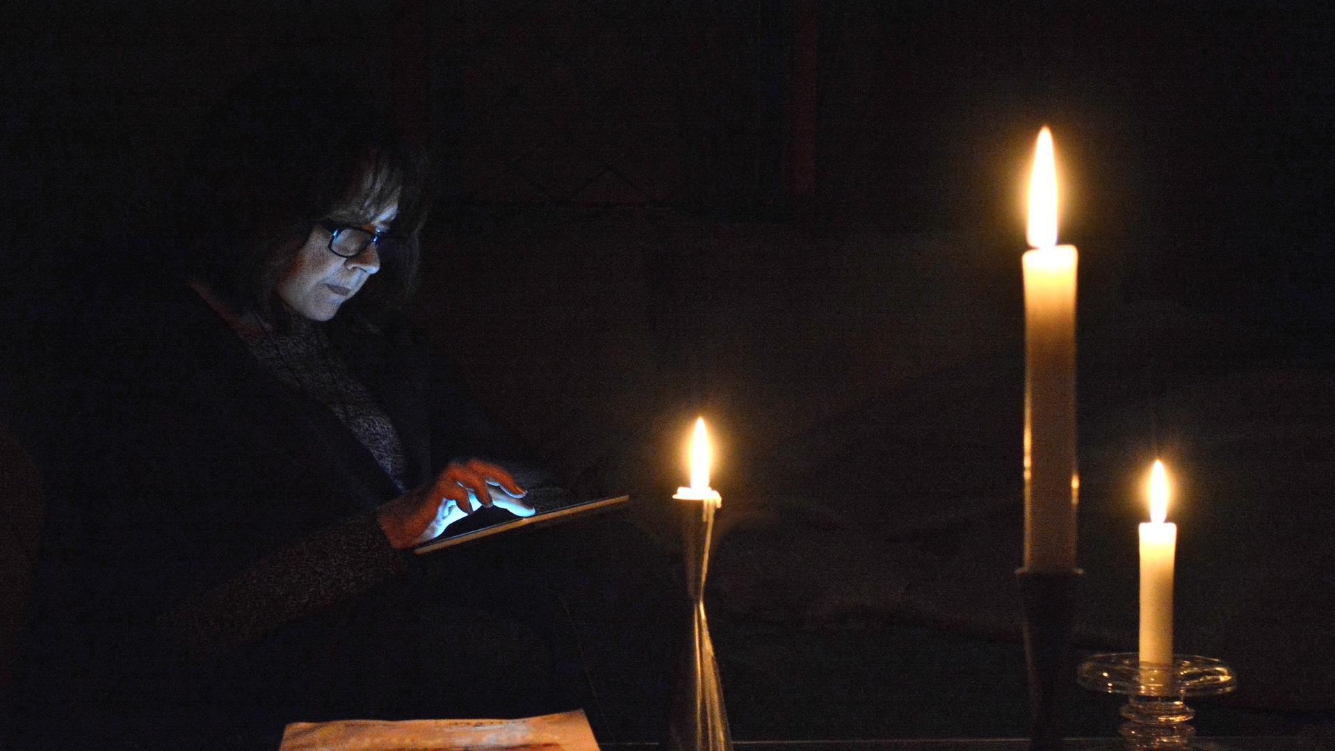 Eine Person guckt bei Dunkelheit und Kerzenschein auf ihr Tablet.