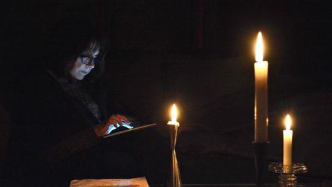 Eine Person guckt bei Dunkelheit und Kerzenschein auf ihr Tablet. Eine Person guckt bei Dunkelheit und Kerzenschein auf ihr Tablet.