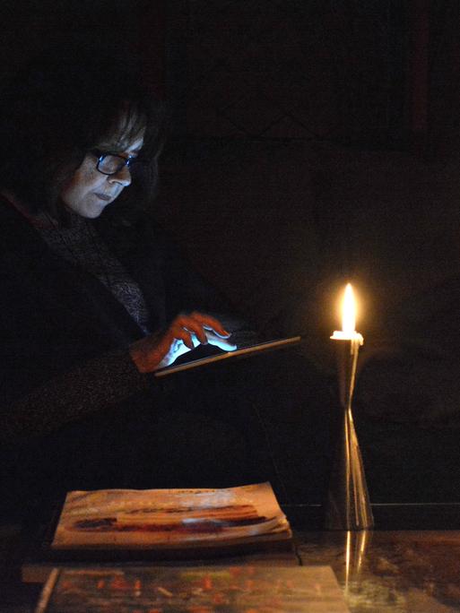 Eine Person guckt bei Dunkelheit und Kerzenschein auf ihr Tablet.
