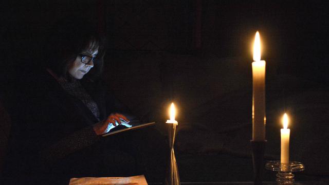 Eine Person guckt bei Dunkelheit und Kerzenschein auf ihr Tablet. Eine Person guckt bei Dunkelheit und Kerzenschein auf ihr Tablet.