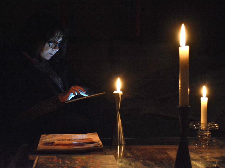 Eine Person guckt bei Dunkelheit und Kerzenschein auf ihr Tablet.