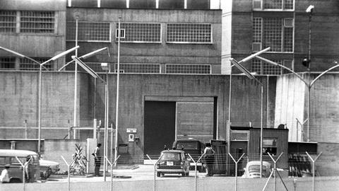 Das Schwarz-Weiß-Foto zeigt ein Betongebäude hinter Stacheldrahtzaun sowie Wachposten, die vor einem Wachhäuschen stehen.  