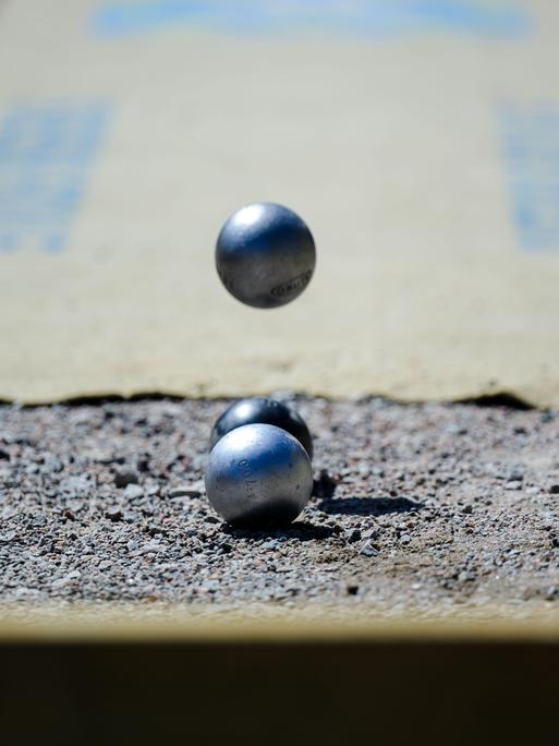 Bei einem Boule-Wettbewerb fließt eine Metallkugel auf zwei liegende Kugeln zu. 