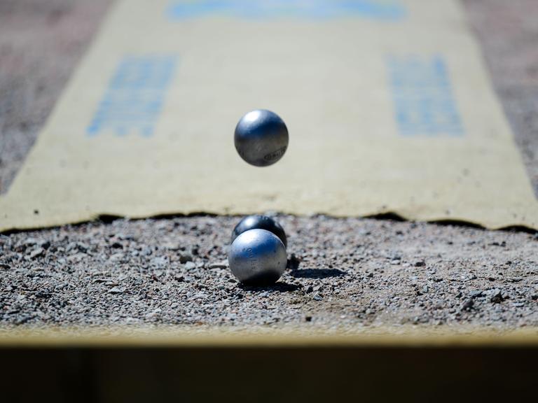 Bei einem Boule-Wettbewerb fließt eine Metallkugel auf zwei liegende Kugeln zu. 