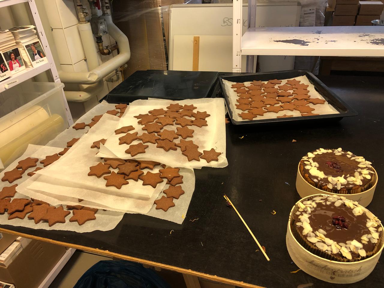 Auf einem Tisch in der Küche stehen zwei Torten und auf Papier liegen Plätzchen in Sternform zum Abkühlen.