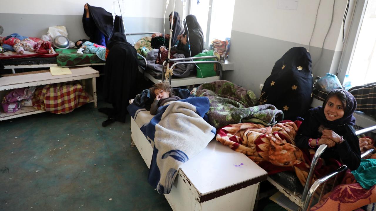 Kinder in einem Krankenhaus in Kabul. Sie liegen unter ärmlichen Decken, mehrere kleine Kinder in einem Bett, mit verhüllten Frauen die daneben sitzen.