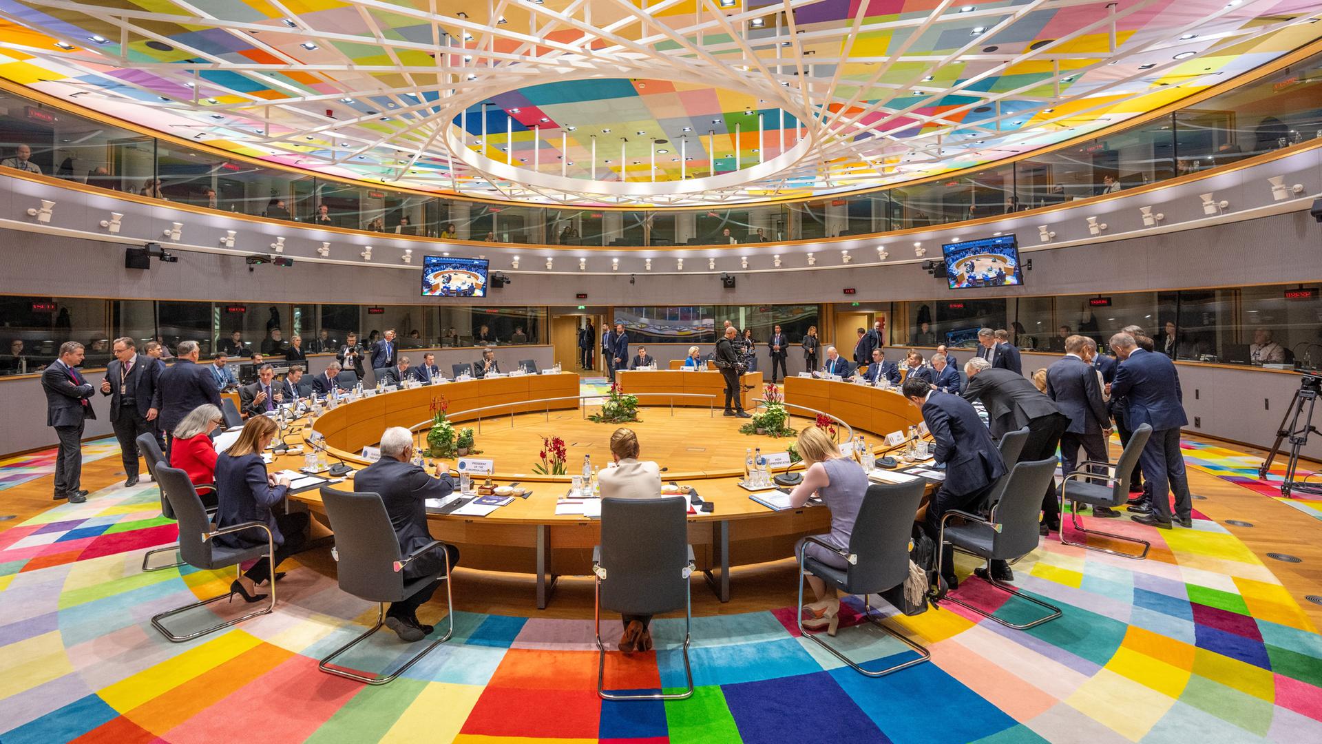Der Sitzungssaal des EU-Gipfeltreffens in Brüssel. Die Sitzanordnung ist im Kreis. Etliche Teilnehmer sitzen und stehen. Boden und Decke sind mit bunten Rechtecken verziert.