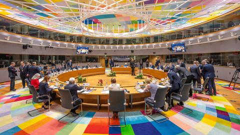 Der Sitzungssaal des EU-Gipfeltreffens in Brüssel. Die Sitzanordnung ist im Kreis. Etliche Teilnehmer sitzen und stehen. Boden und Decke sind mit bunten Rechtecken verziert.