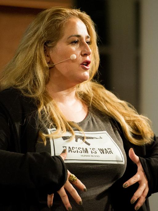 Die Kabarettistin Idil Baydar trägt ein Helikopter-Mikrofon und ein T-Shirt mit der Aufschrift "Racism is war".