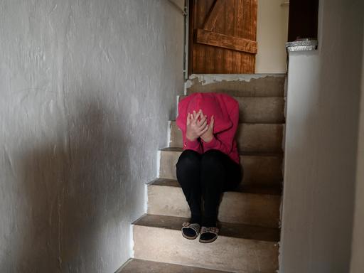 Symbolfoto: Frau sitzt zusammengekauert auf Treppe.