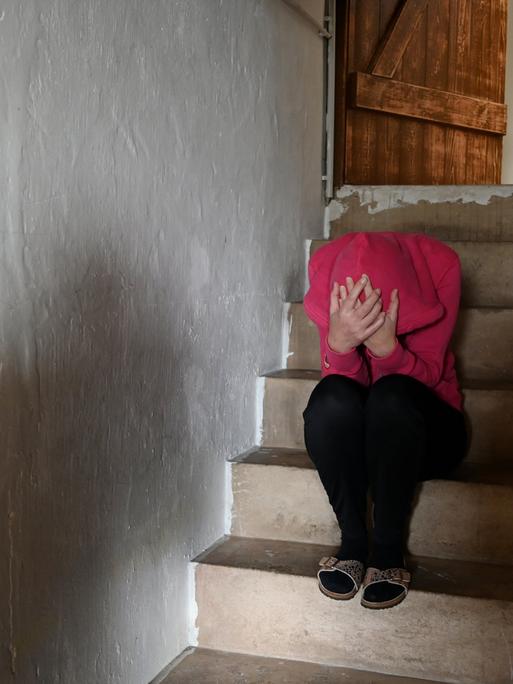 Symbolfoto: Frau sitzt zusammengekauert auf Treppe.