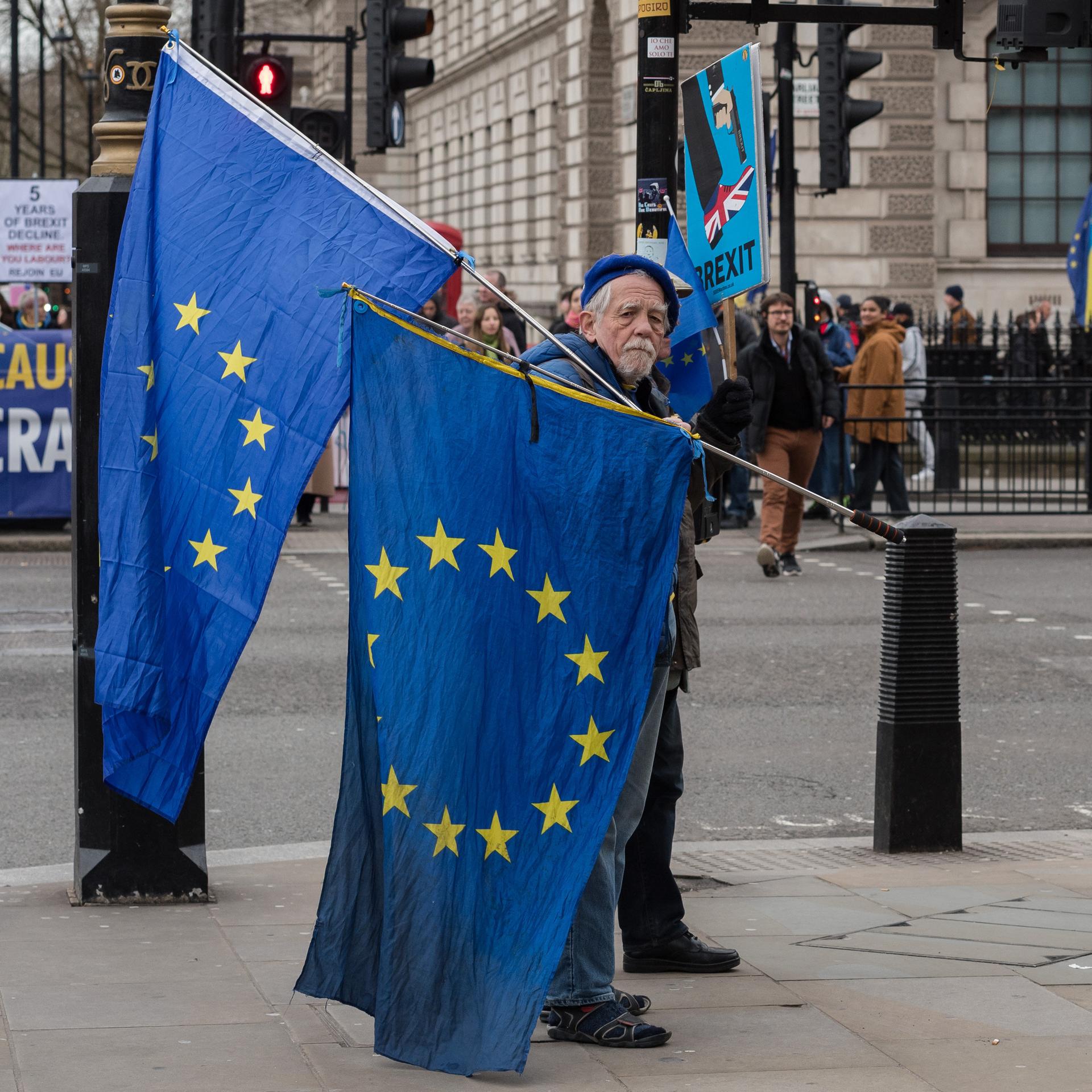 Ein alter Mann trägt in einer Londoner Straße zwei EU-Fahnen zum Protest gegen den Brexit. 