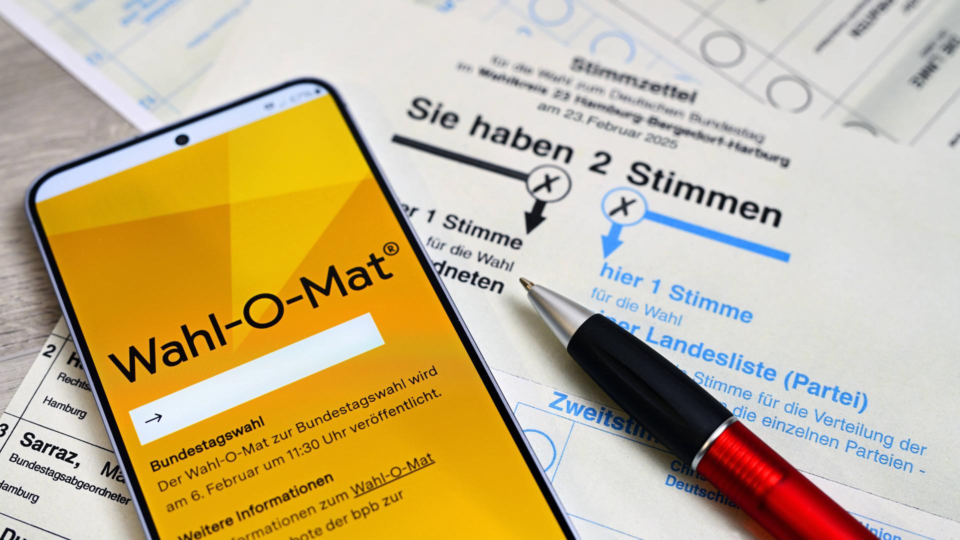 Wahl-O-Mat auf einem Smartphone und ein Stift liegen auf einem Stimmzettel zur Bundestagswahl