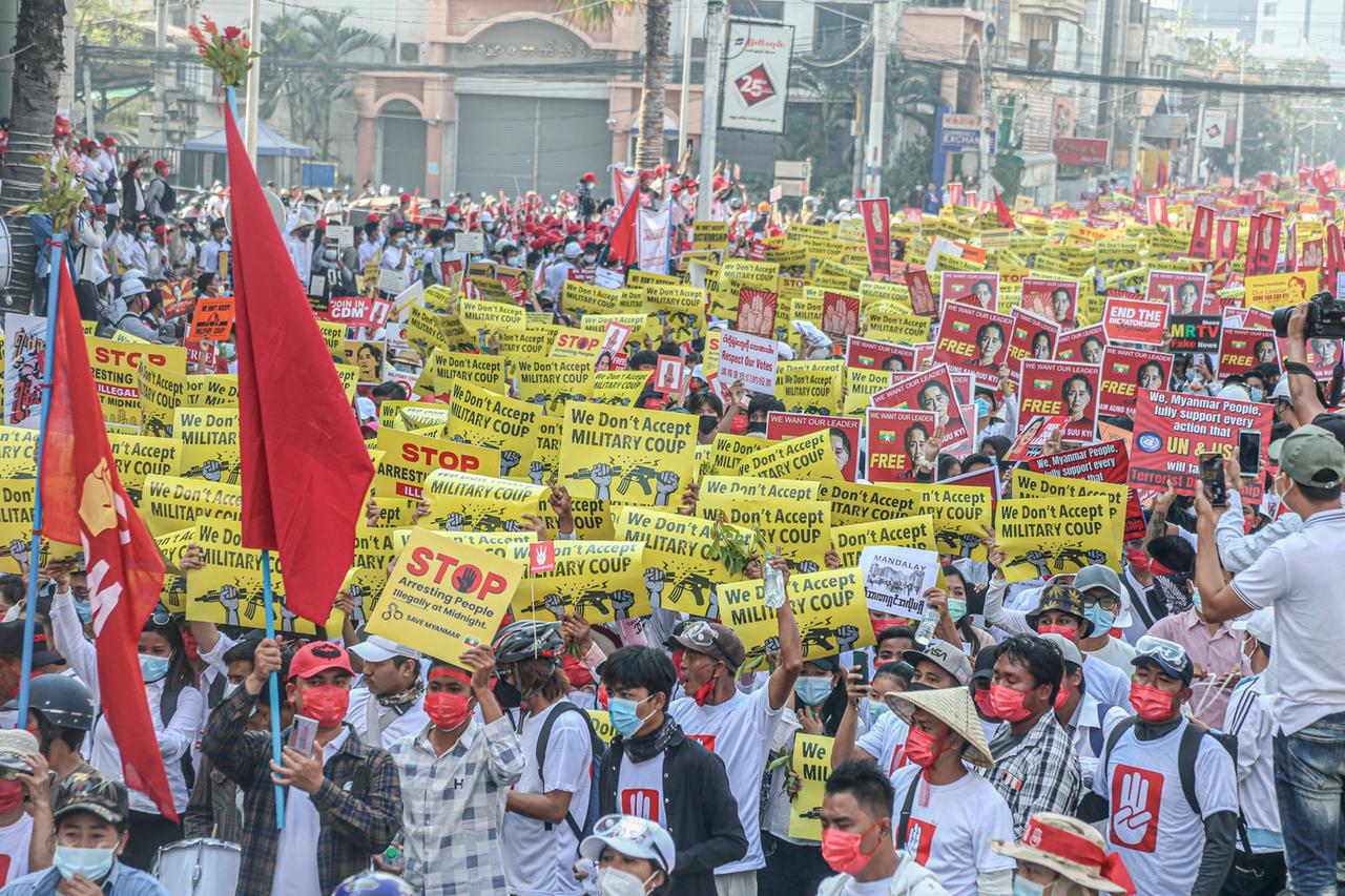 Tausende Menschen laufen in der Stadt Mandalay mit Protesplakaten eine Straße entlang.