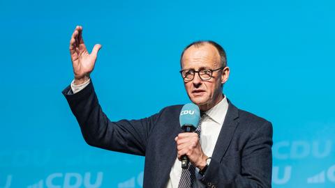 Friedrich Merz spricht auf der Bühne vor blauem Hintergrund.