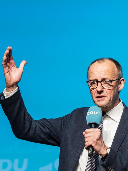 Friedrich Merz spricht auf der Bühne vor blauem Hintergrund.