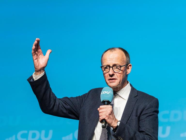 Friedrich Merz spricht auf der Bühne vor blauem Hintergrund.