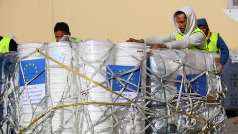 Mehrere Männer in gelben Warnwesten hantieren an mit Stricken zusammengebundenen weißen Säcken.