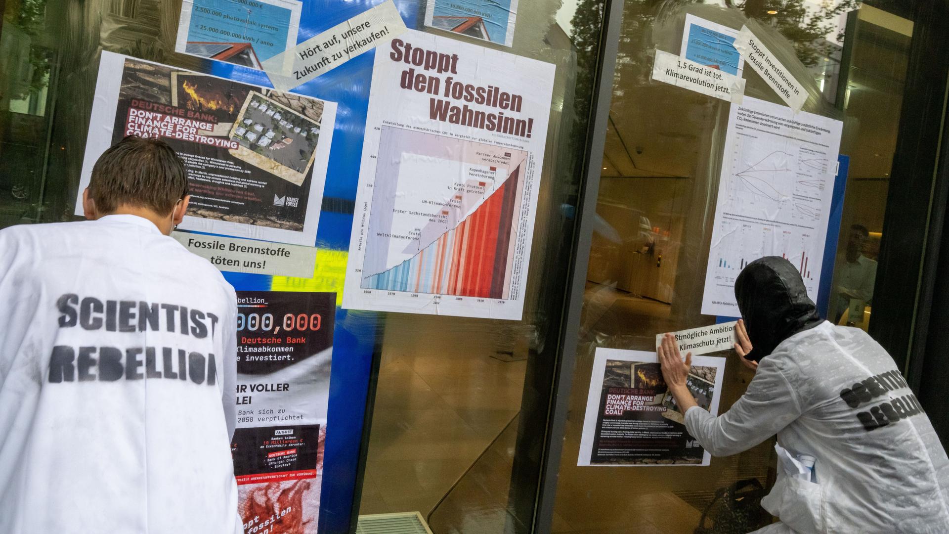 Aktivisten der Klimabewegung "Scientist Rebellion" kleben Plakate mit Fakten über die Erderwärumg an eine Filiale der Deutschen Bank in München. 