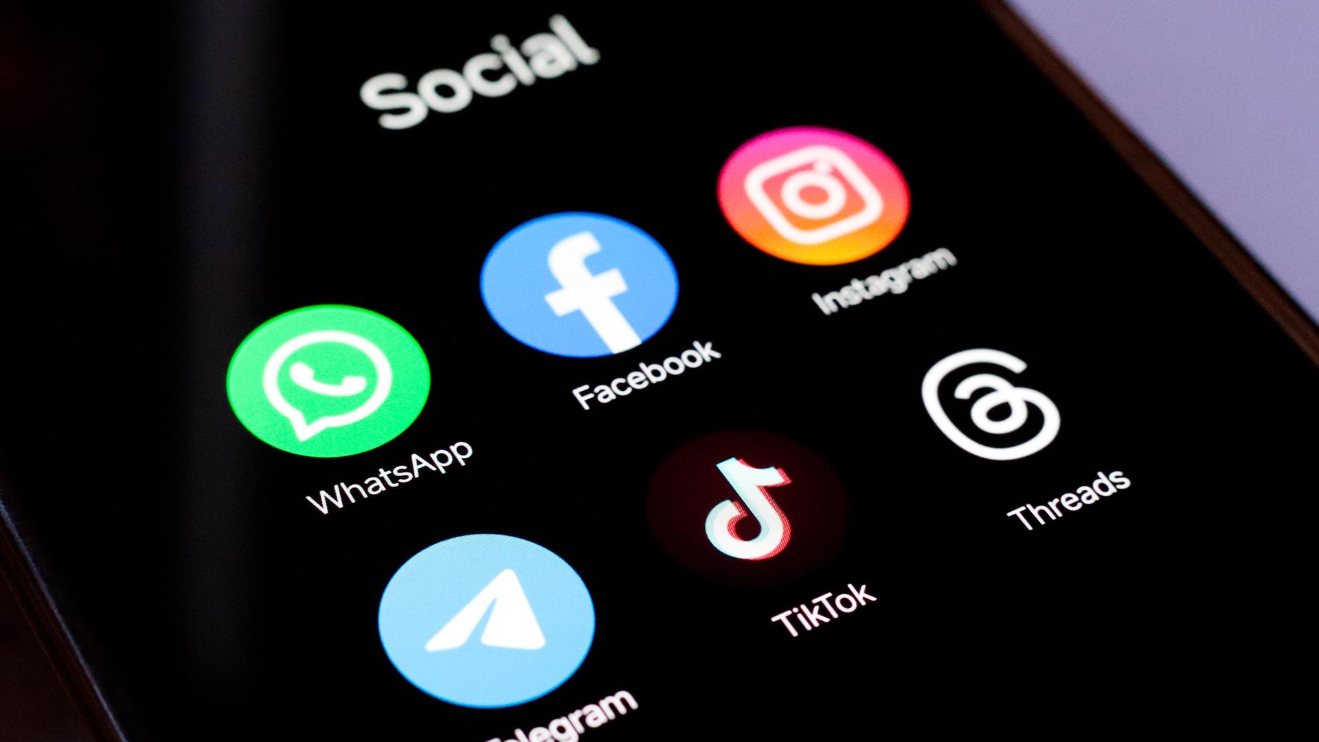 Auf einem Smartphone-Bildschirm sind die Logos der Online-Plattformen Whatsapp, Facebook, Instagram, Telegram, Tiktok und Threads abgebildet.