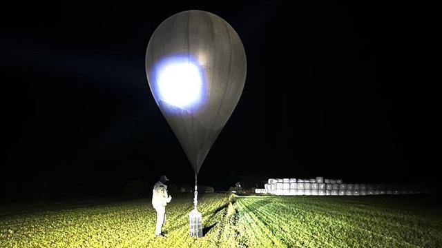 Nachtaufnahme eines Wetterballons auf einem Feld, an dessen Ende ein Paket mit Zigaretten befestigt ist