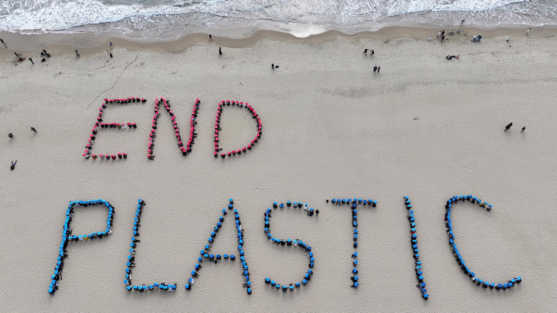 An einem Strand sind die Worte END PLASTIC mit Plastikmüll in den Sand gelegt worden