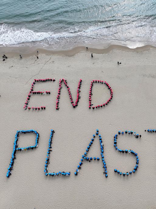 An einem Strand sind die Worte END PLASTIC mit Plastikmüll in den Sand gelegt worden