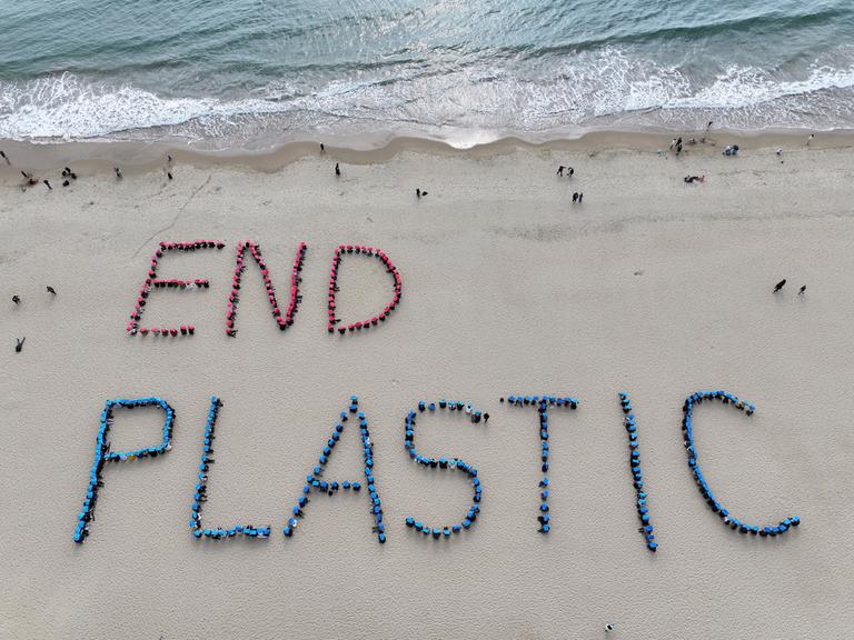 An einem Strand sind die Worte END PLASTIC mit Plastikmüll in den Sand gelegt worden