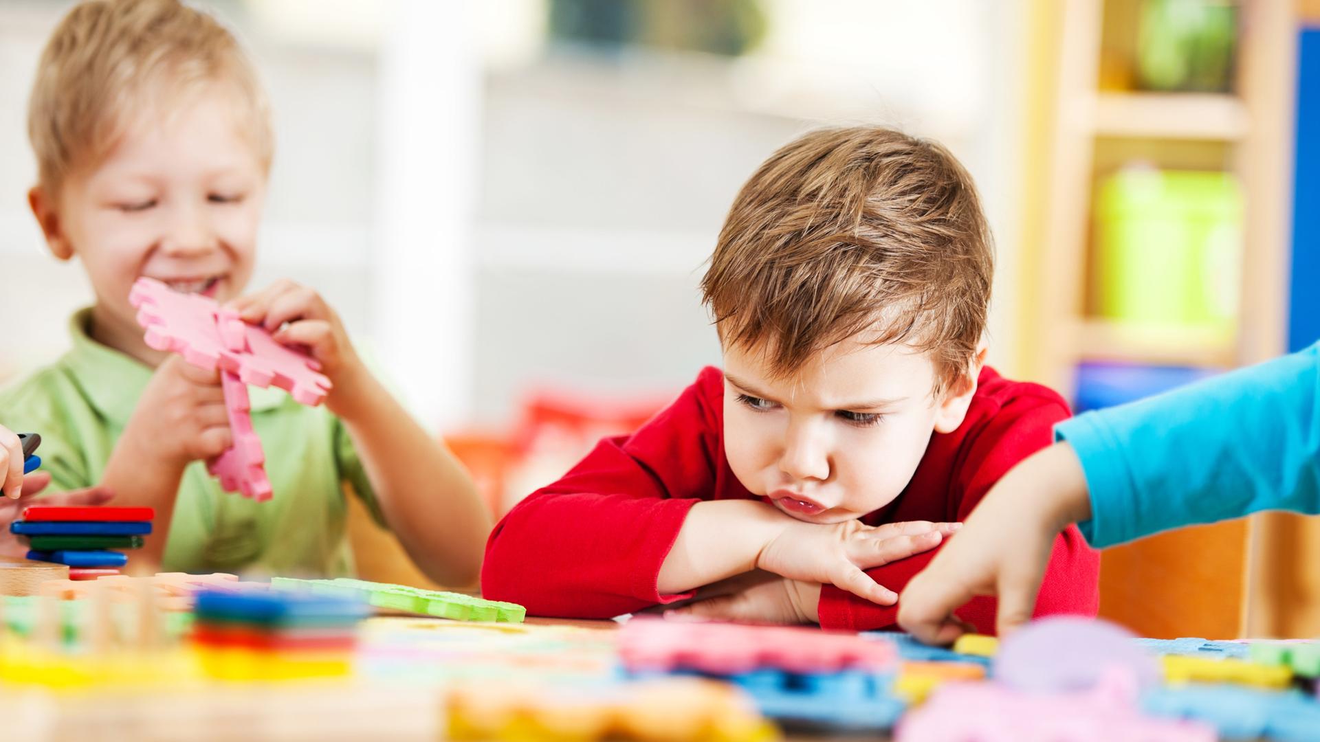 Ein kleiner Junge im Kindergarten schaut mit frustriertem Blick auf sein Puzzle.