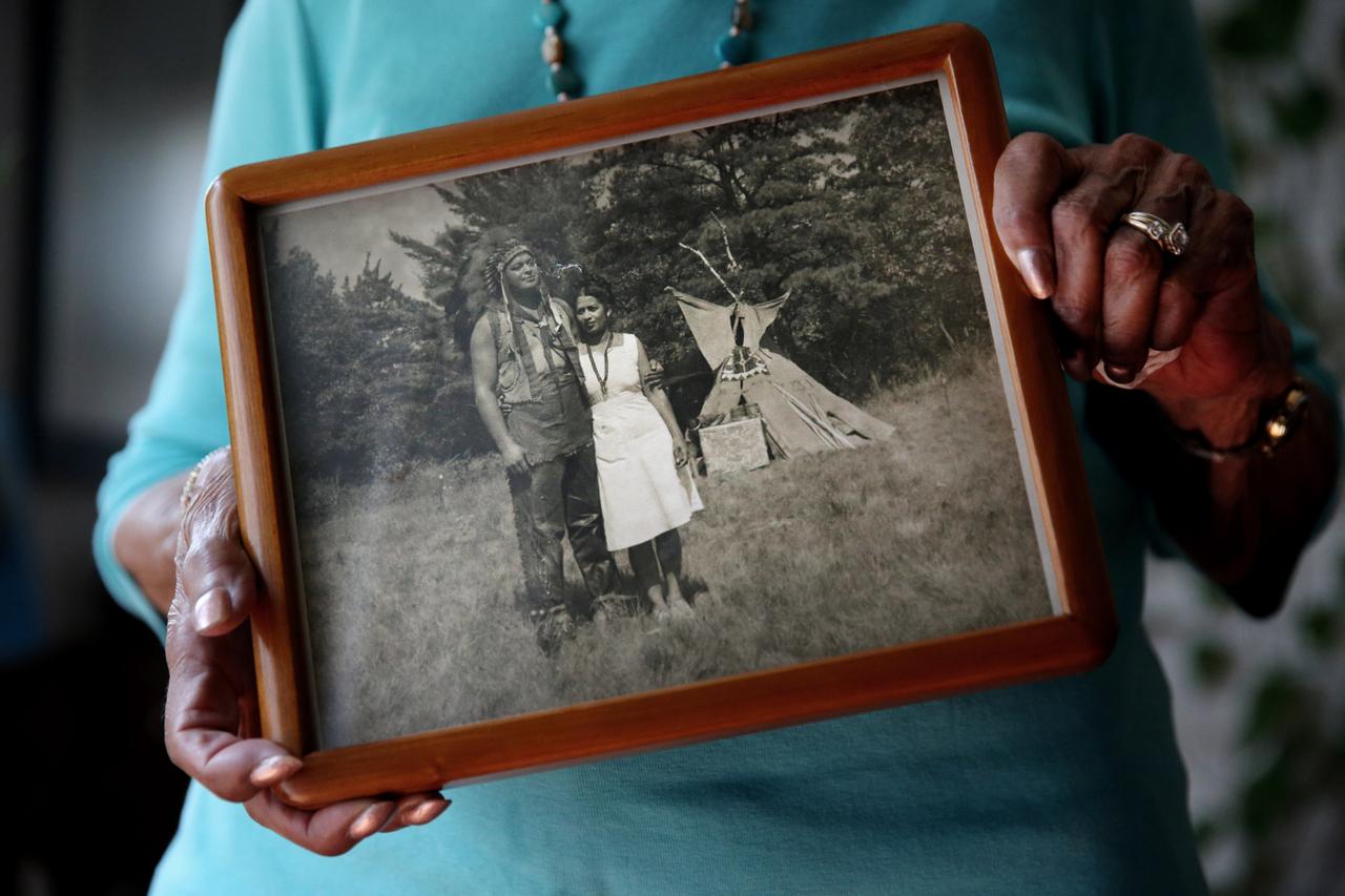 Eine Person hält einen Bilderrahmen mit einem Foto in der Hand, auf dem Bild sieht man ein junges Native American Paar vor einem Tipi.