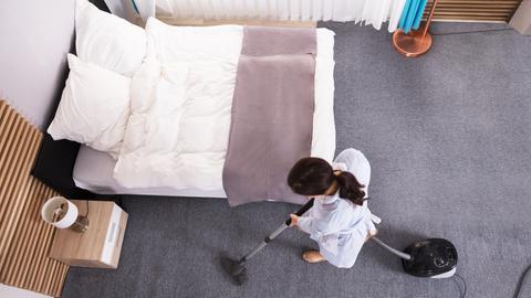 Eine Person saugt ein Hotelzimmer. Die Aufnahme ist von oben aus der Vogelperspektive gemacht.